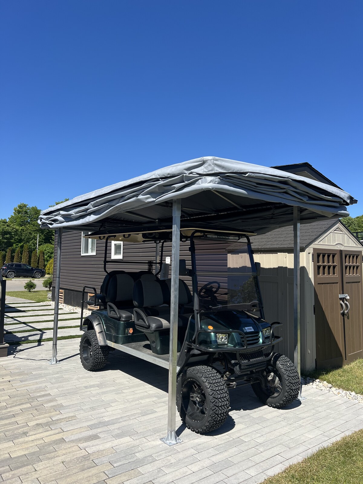 6-seater customized golf cart under Touchless Cover canopy beside storage shed on paver driveway
